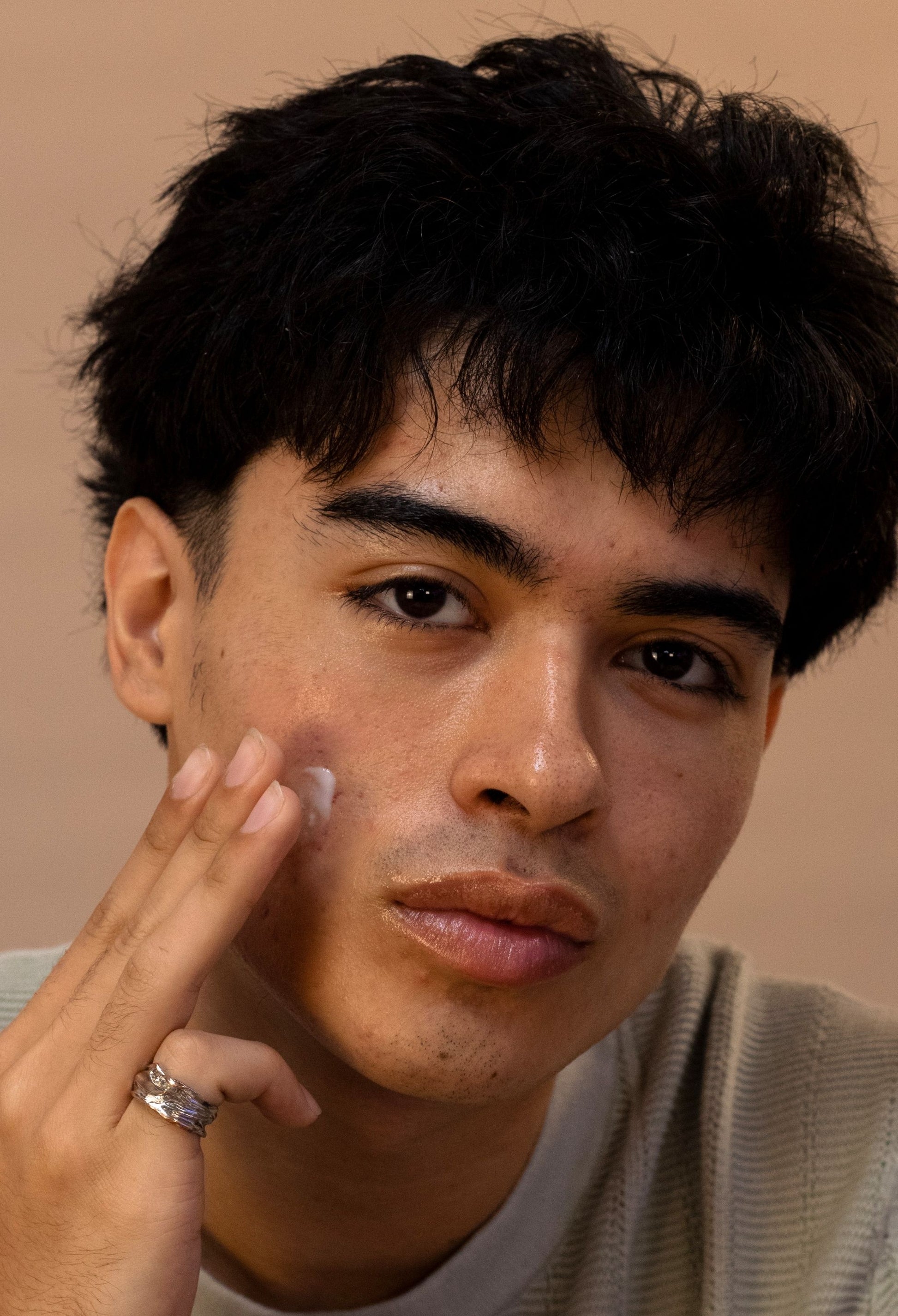 Man with dark hair and thick eyebrows applying Space Face Moisturizer by Saturn Skin to his face with a neutral background