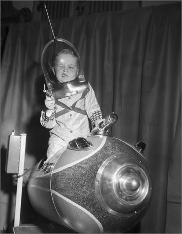 Vintage photo of a young boy wearing an astronaut costume and pointing a toy space gun while sitting in a spaceship ride